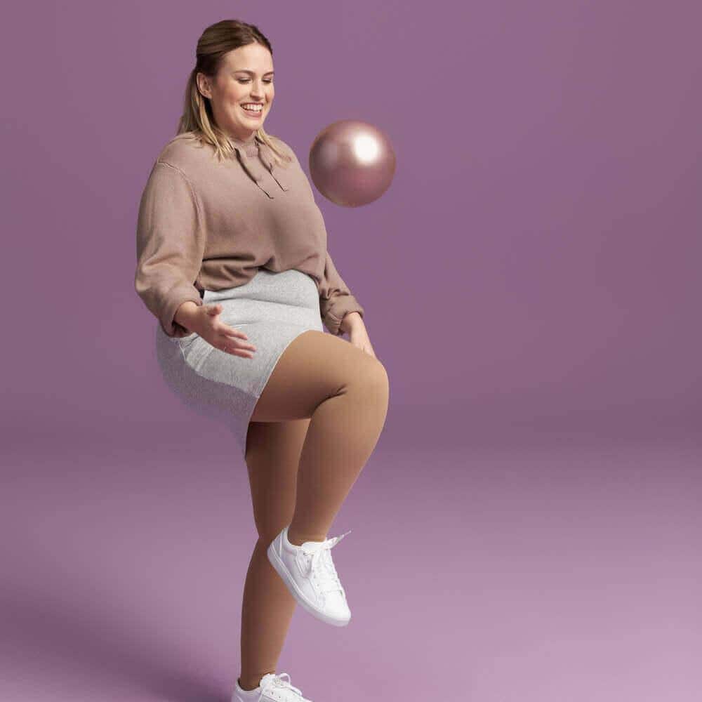 VenoTrain® delight 2 A lively woman with a toy ball against a purple studio backdrop, in a relaxed pose and looking cheerful.