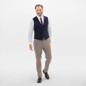 Professionele man in net pak met gilet en das, wandelend voor een lichte, neutrale achtergrond.